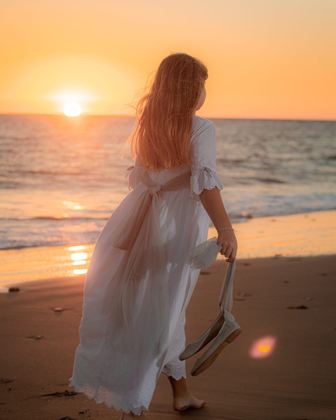 Niña de comunión descalza en la orilla al atardecer